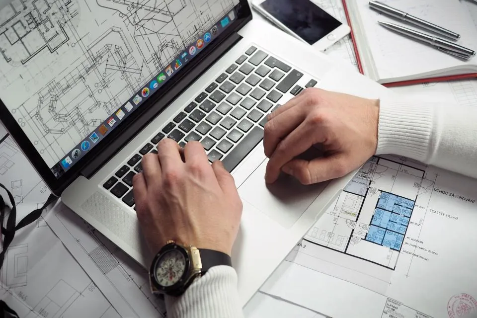 Hands on a laptop keyboard beside architectural plans
